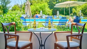 Een tafel bij het zwembad met twee Corona Extra flessen, twee houten stoelen en uitzicht op een zwembad en groen.