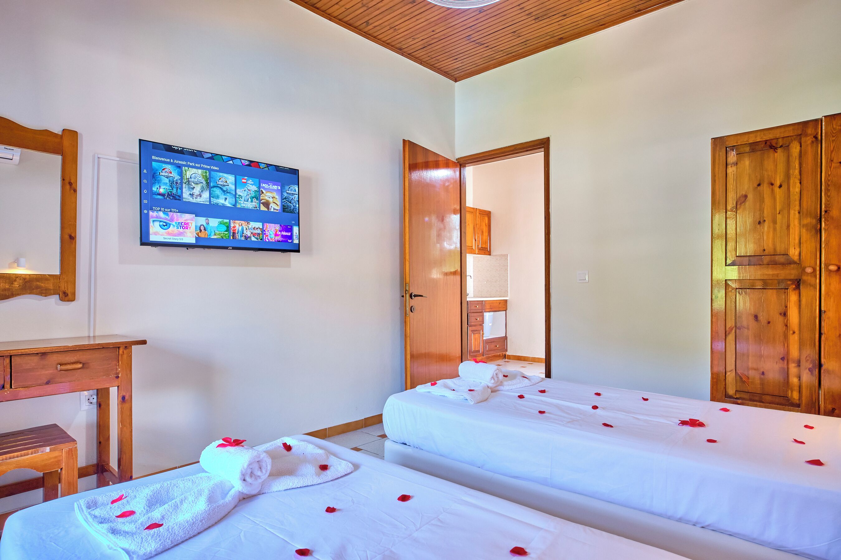 Une chambre d’hôtel avec deux lits, un téléviseur fixé au mur, un bureau en bois et une armoire en bois.