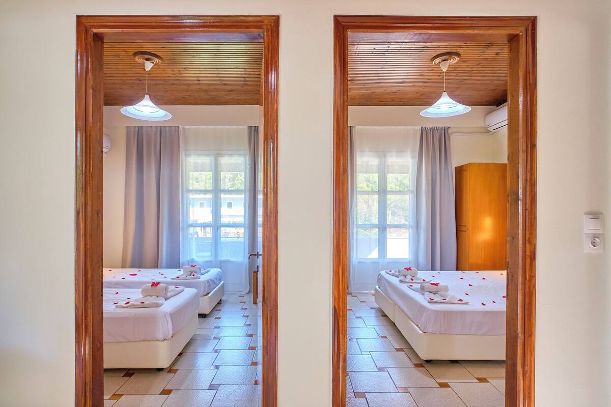 A mirrored view of a hotel room with two beds, a wooden ceiling, and a large window.