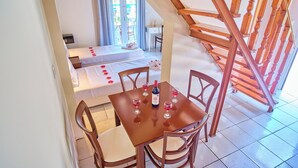Hotelkamer met een houten trap, een eettafel met wijnglazen en twee bedden met rode bloemen.