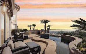 A rooftop patio with outdoor furniture, a pool, and a sunset view.