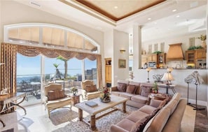 A spacious living room with a large window, a balcony, and a kitchen area.