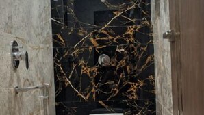 A bathroom with a marble wall, a toilet, and a shower area. - Shree Dhara Heaven (Varanasi)