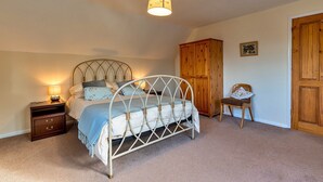 A bedroom with a bed, nightstand, wooden wardrobe, and a chair. - Cottage in Wellington near Blackdown Hills (Wellington)