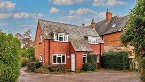 A red brick house with a sloped roof, a front door, and a small porch. - Cottage in Wellington near Blackdown Hills (Wellington)