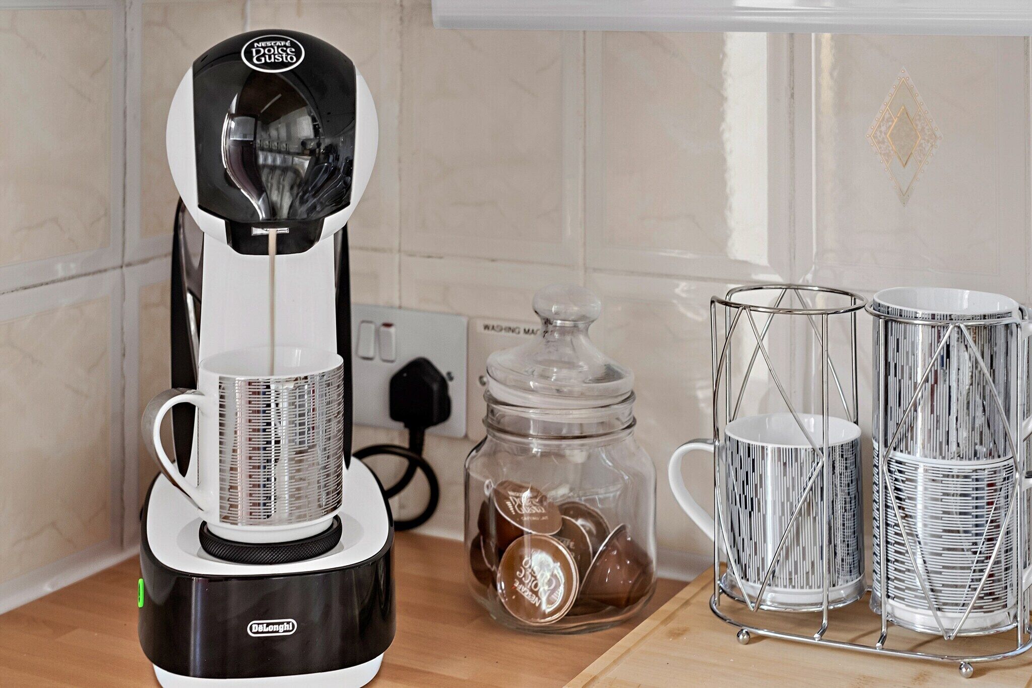 A kitchen with a coffee maker, a jar of coffee pods, and two metal coffee dispensers.