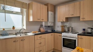 A modern kitchen with wooden cabinets, a gas stove, a sink, and a small dining table with two glasses of orange juice. - Apartment in Llanberis near Snowdonia Park (Llanberis)