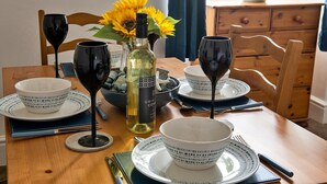 A dining table set with white and blue patterned bowls, plates, and wine glasses, accompanied by a bottle of white wine and a vase with sunflowers. - Apartment in Llanberis near Snowdonia Park (Llanberis)