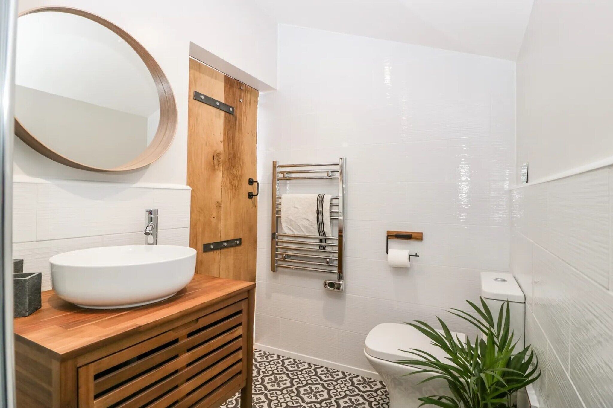 Un baño con tocador de madera, un espejo redondo, toallero y retrete.