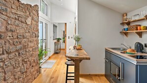 Una cocina moderna con una mesa de madera, taburetes de bar, una pared de ladrillo y vistas al área de comedor.