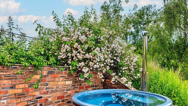 Una bañera de madera junto a un muro de ladrillo con plantas en flor.
