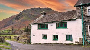 A white building with green windows and a stone chimney, numbered 1688, set against a mountainous backdrop. - Cottage in Grasmere near Lake & Scenic Trails (Grasmere)