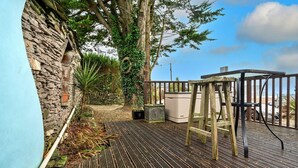 Um deck de madeira com um muro de pedra, uma escada de madeira e um aquecedor de exterior branco.