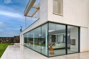 A modern house with large glass windows, a stone wall, and a lawn. - Clifftop Retreat in Criccieth with Stunning Views (Criccieth)
