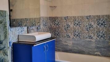 Un baño moderno con bañera, un mueble azul, inodoro y zona de ducha.
