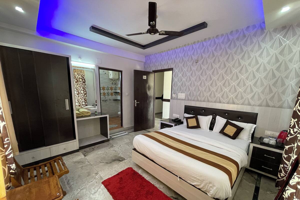 A modern hotel room with a large bed, a desk, a wardrobe, and a bathroom visible through an open door.