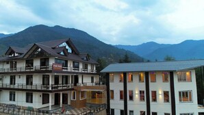 A multi-story hotel with a sign reading "Pink Park Hotel Restaurant" and a view of mountains in the background. - Pink Park By Panache Hotel (Bir)