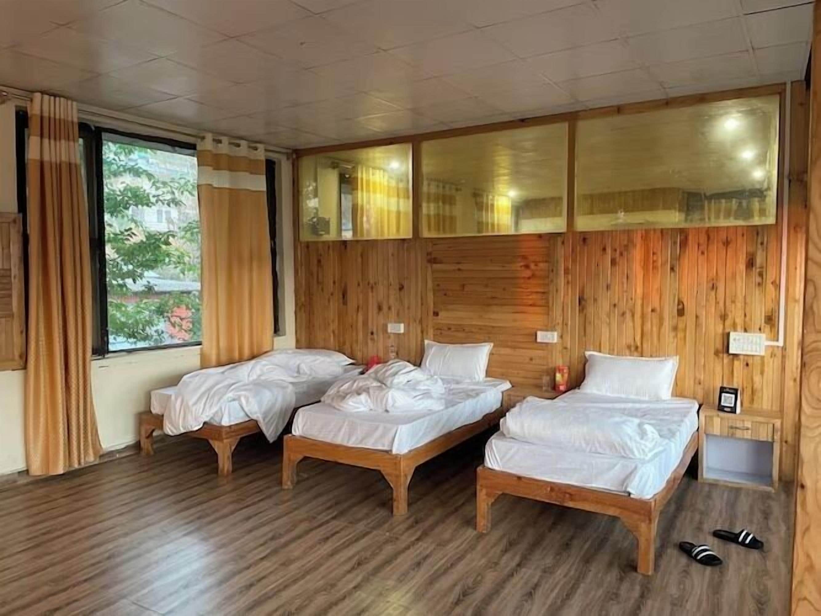 Una habitación con tres camas de madera, una ventana con cortinas y un par de pantuflas en el suelo.