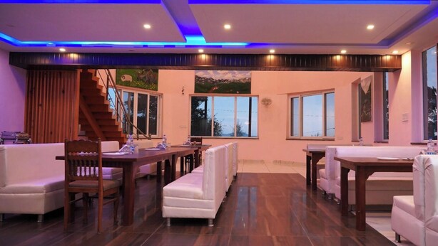 A spacious living area with a wooden floor, white sofas, and a dining table. There are large windows providing natural light and views of the outdoors. - Pink Park By Panache Hotel (Bir)