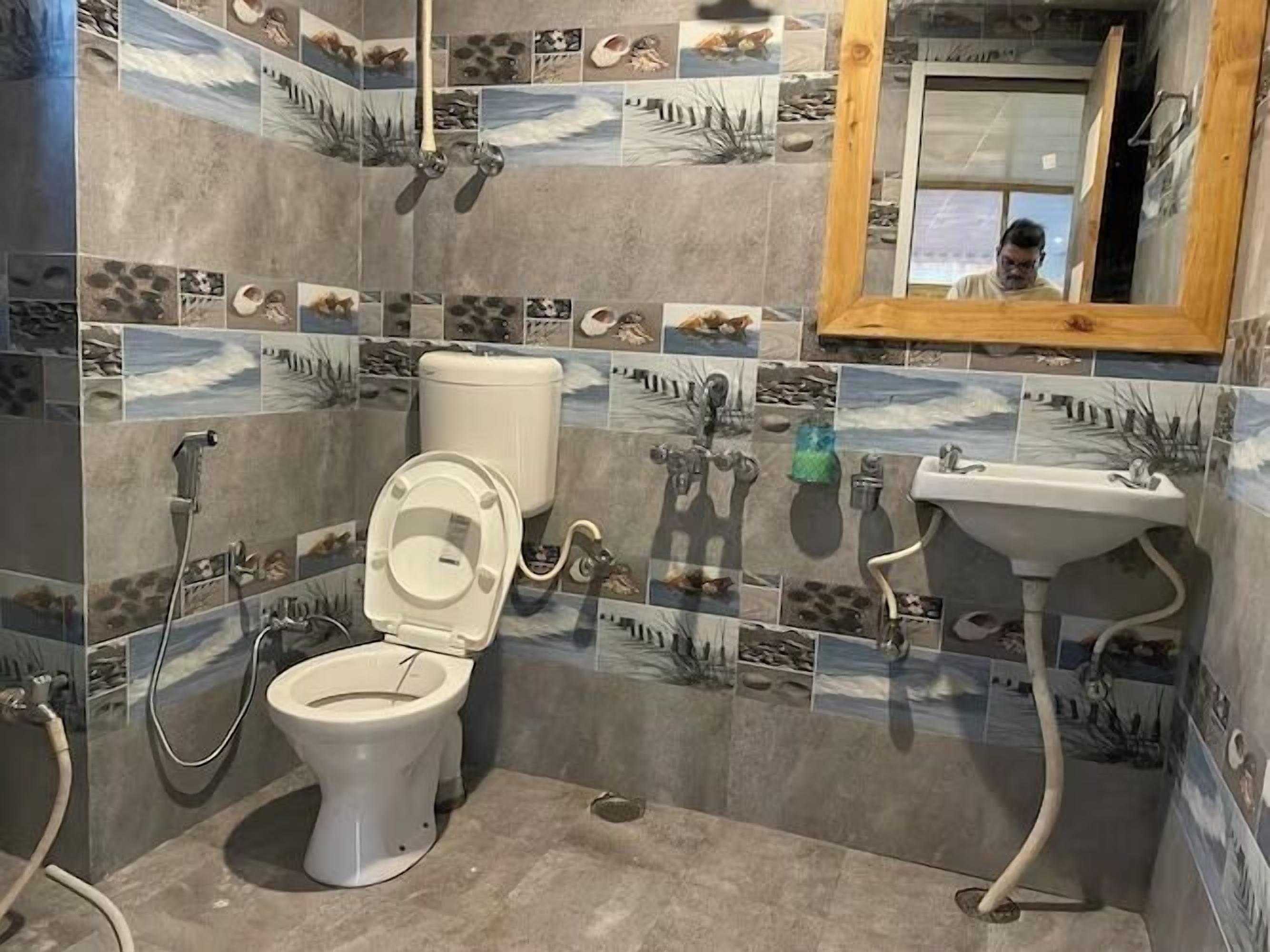 Baño con inodoro, ducha y lavamanos, con mosaico de temática natural.