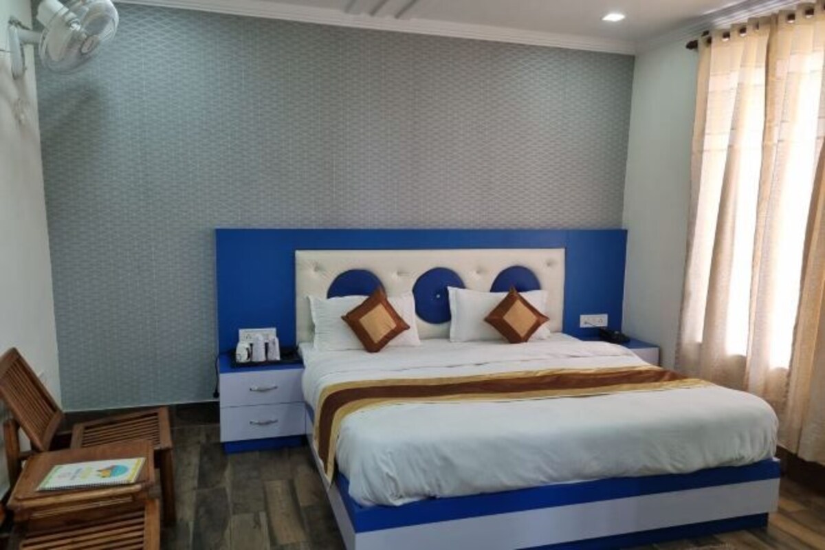 A neatly arranged hotel room with a large bed, a bedside table, a chair, and a small table with a book.