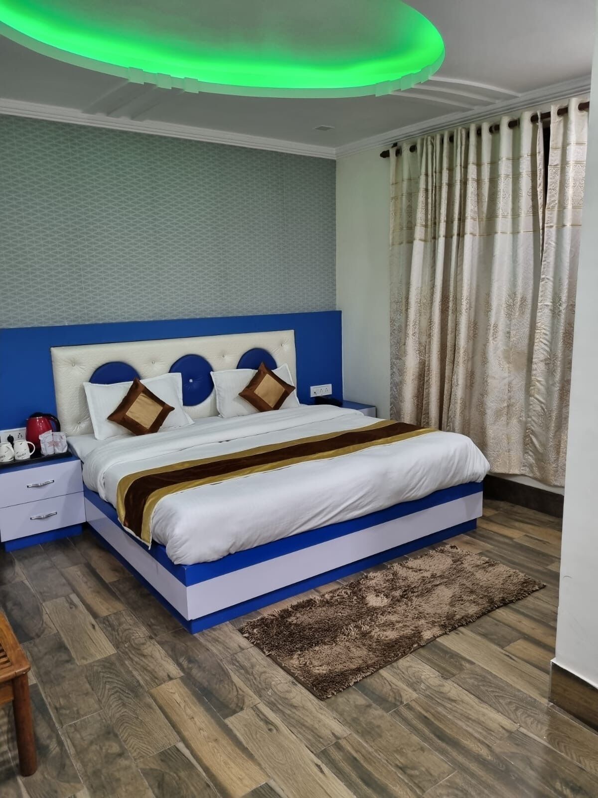 Un dormitorio moderno con una cama azul y blanca, una mesita de noche de madera y una alfombra estampada.