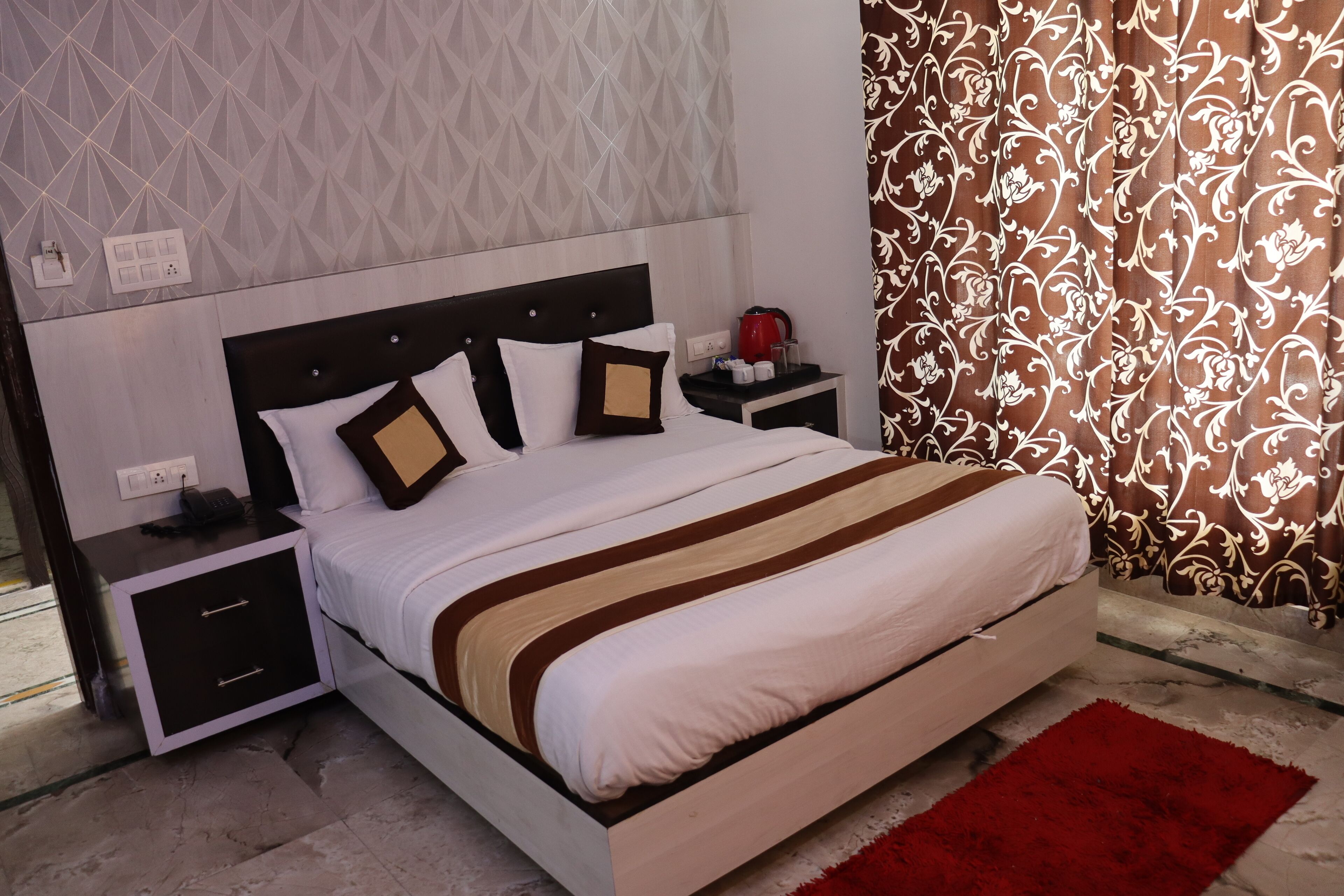 A neatly made bed with a striped bedspread, a nightstand with a red kettle, and patterned curtains.
