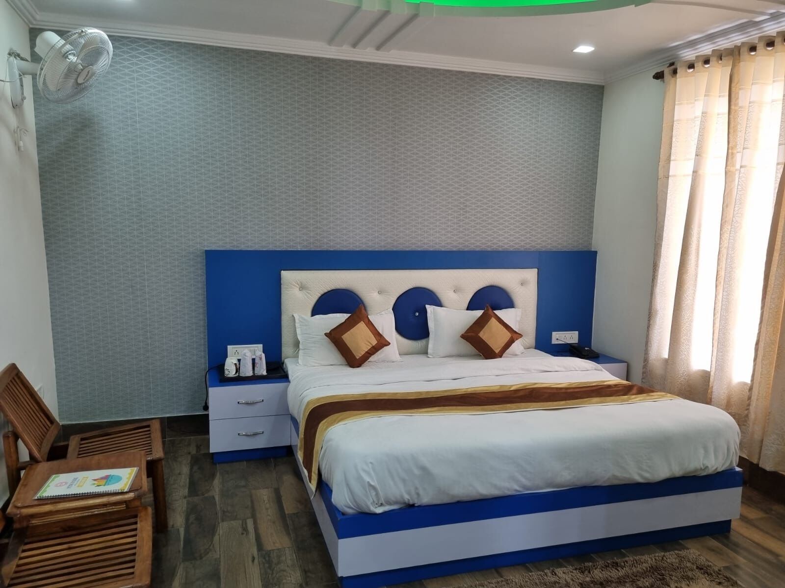 A bedroom with a bed, nightstands, a fan, a chair, and a window with curtains.