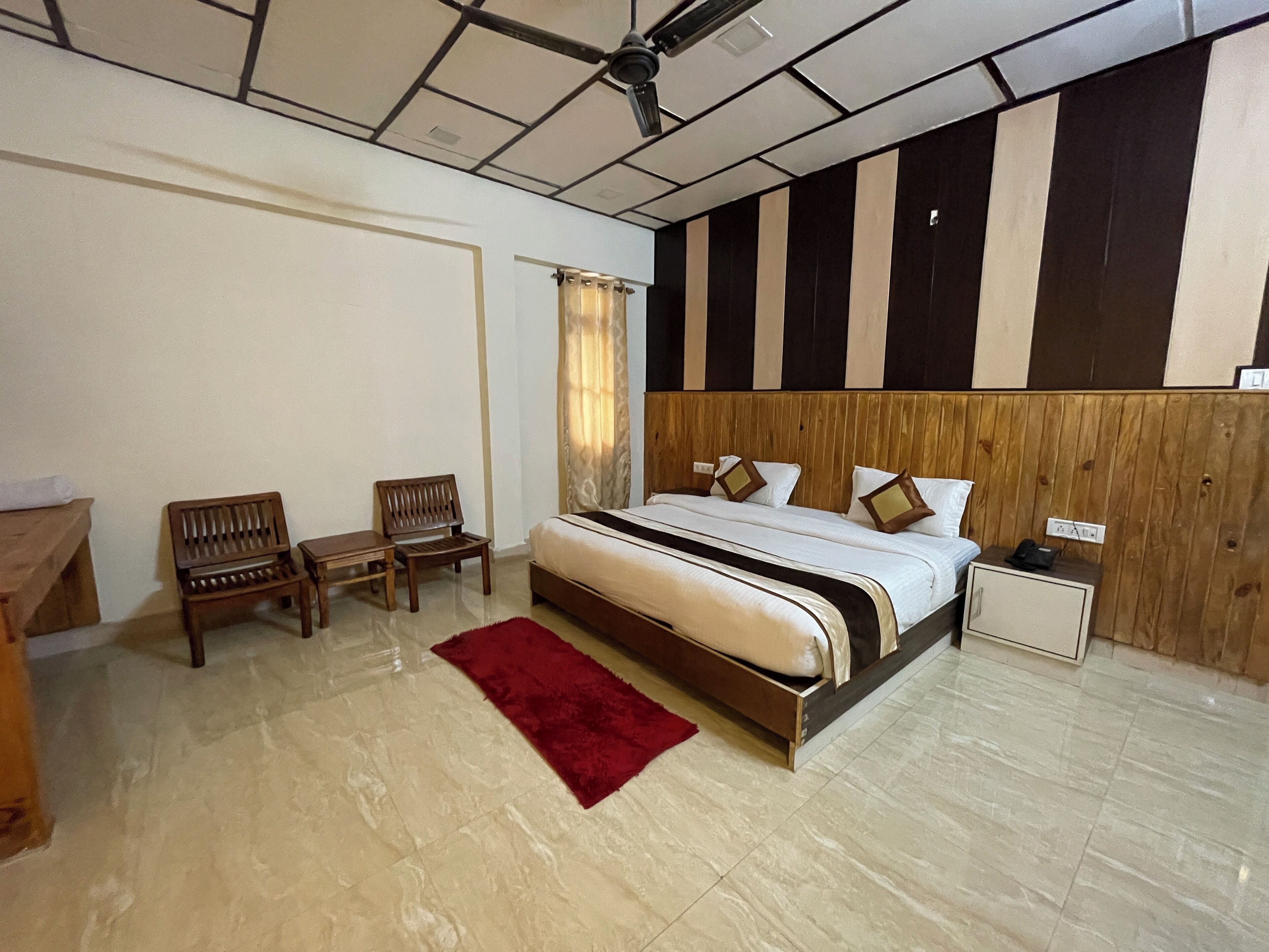 Un dormitorio con una cama grande, dos sillas de madera, un tapete rojo, una mesita de noche y un cabecero de madera.