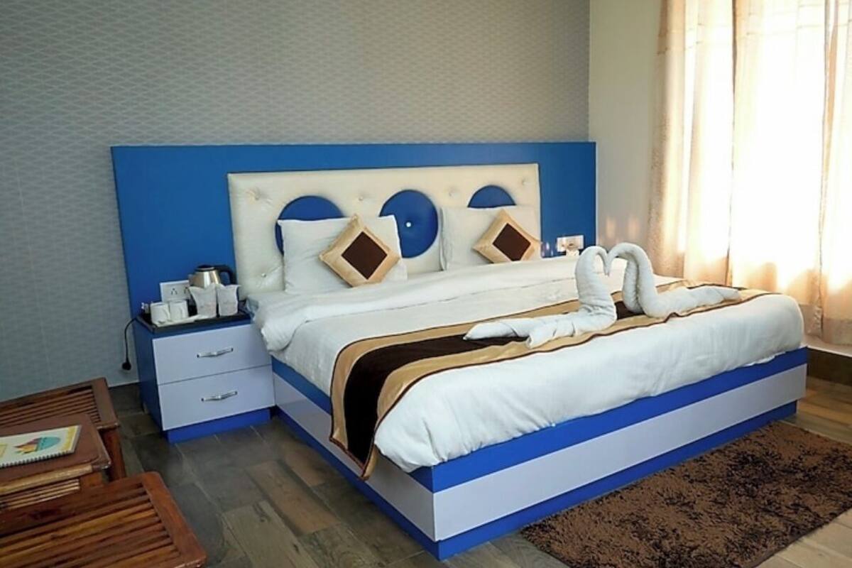 A neatly made bed with a blue headboard, a bedside table with a lamp, and a brown rug on the floor.