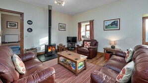 A cozy living room with leather sofas, a wooden coffee table, a fireplace, a television, and framed pictures on the walls.