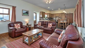 A spacious living room with leather sofas, a wooden coffee table, and a kitchen in the background.