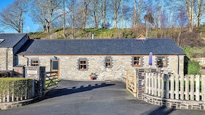 A stone building with a slate roof, a gated entrance, and a small garden area.