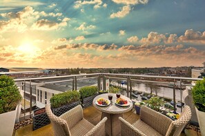 A balcony with wicker furniture, a table with plates of food, and a view of a cityscape and river. - Penthouse in York with River Ouse Views (York)