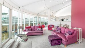 A spacious living area with large windows, a pink sofa set, and a modern chandelier. - Penthouse in York with River Ouse Views (York)