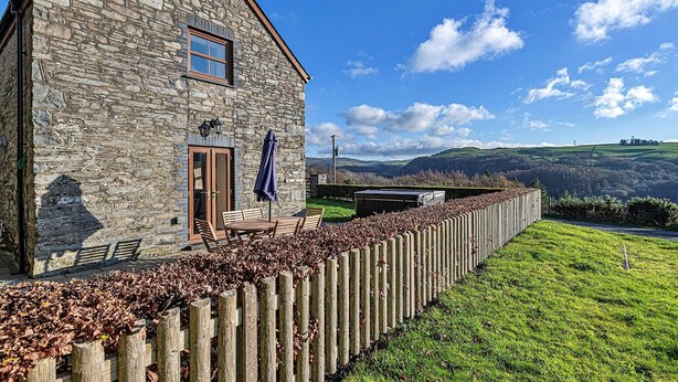 A stone building with a wooden deck, a bench, and a view of rolling hills.