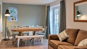 A dining area with a round wooden table, chairs, and a bench. There is a brown sofa with striped pillows and a large mirror on the wall. - Charming Retreat in Cornwall near Bude Beaches (Marhamchurch)