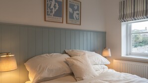 A bedroom with a bed, two wall-mounted lamps, and two framed artworks. - Charming Retreat in Cornwall near Bude Beaches (Marhamchurch)
