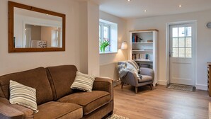 A living room with a brown sofa, a grey armchair, a bookshelf, and a white door. - Charming Retreat in Cornwall near Bude Beaches (Marhamchurch)