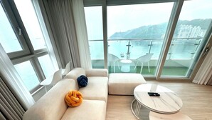 A modern living room with a sofa, ottoman, and two marble coffee tables. Large windows offer a view of a body of water and distant buildings. - THE DECEMBER STAY Busan Ocean Terrace (Busan)