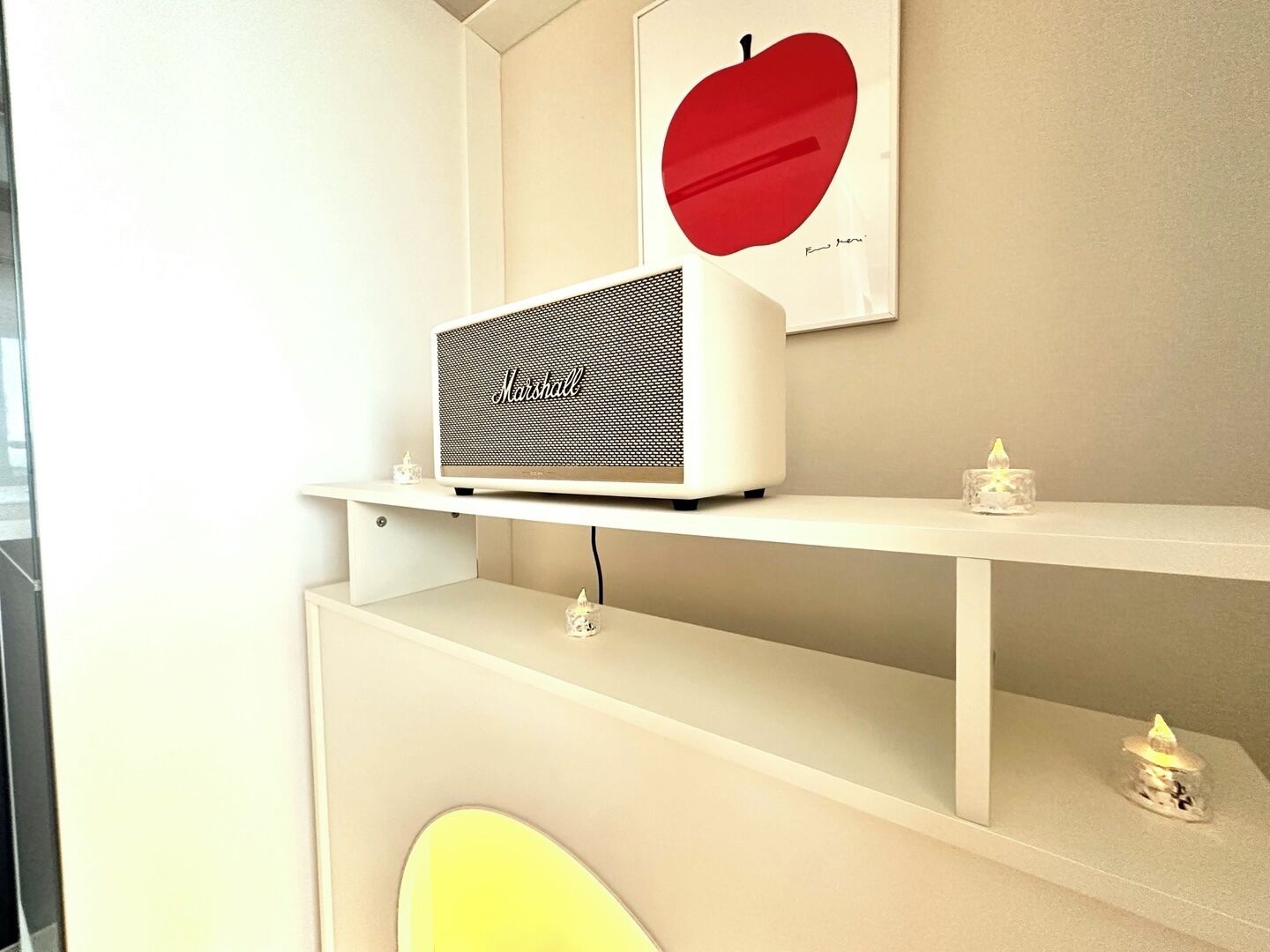 A white Marshall speaker on a shelf with a red apple artwork above it.