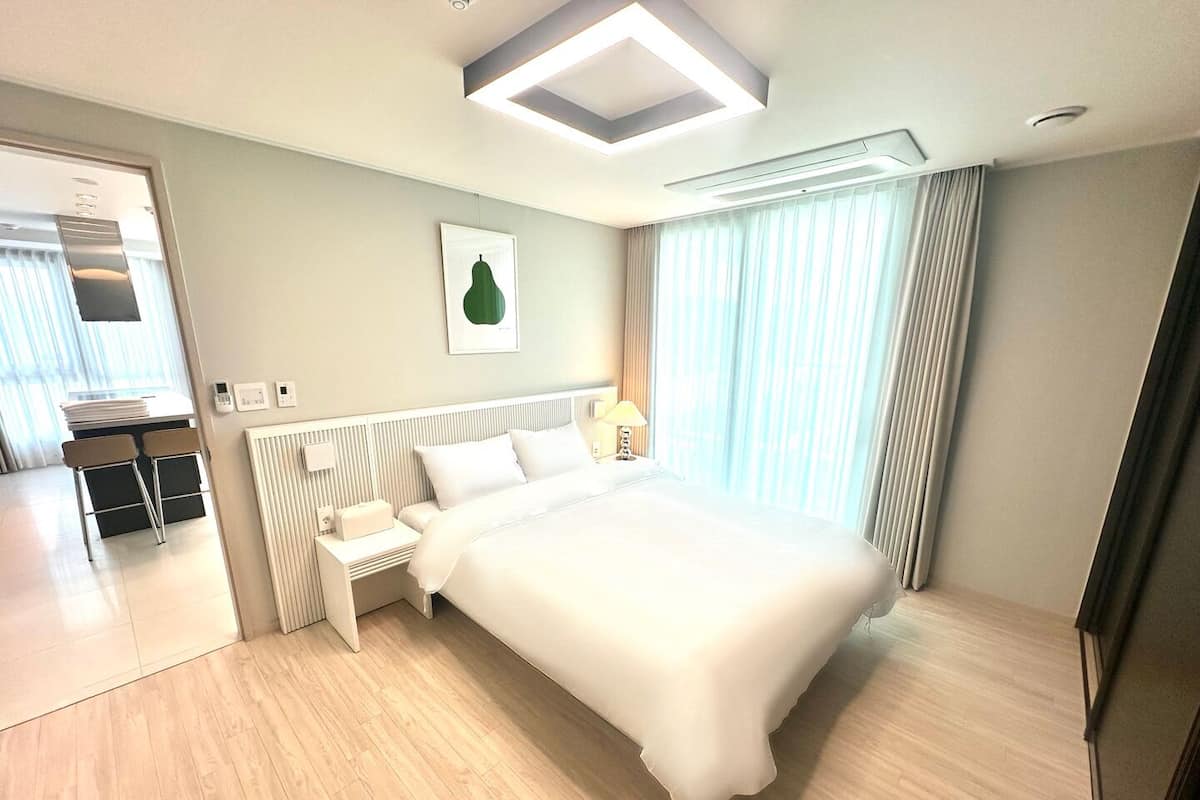 Una habitación de hotel moderna con una cama grande, una mesita de noche, una lámpara y una ventana con cortinas.