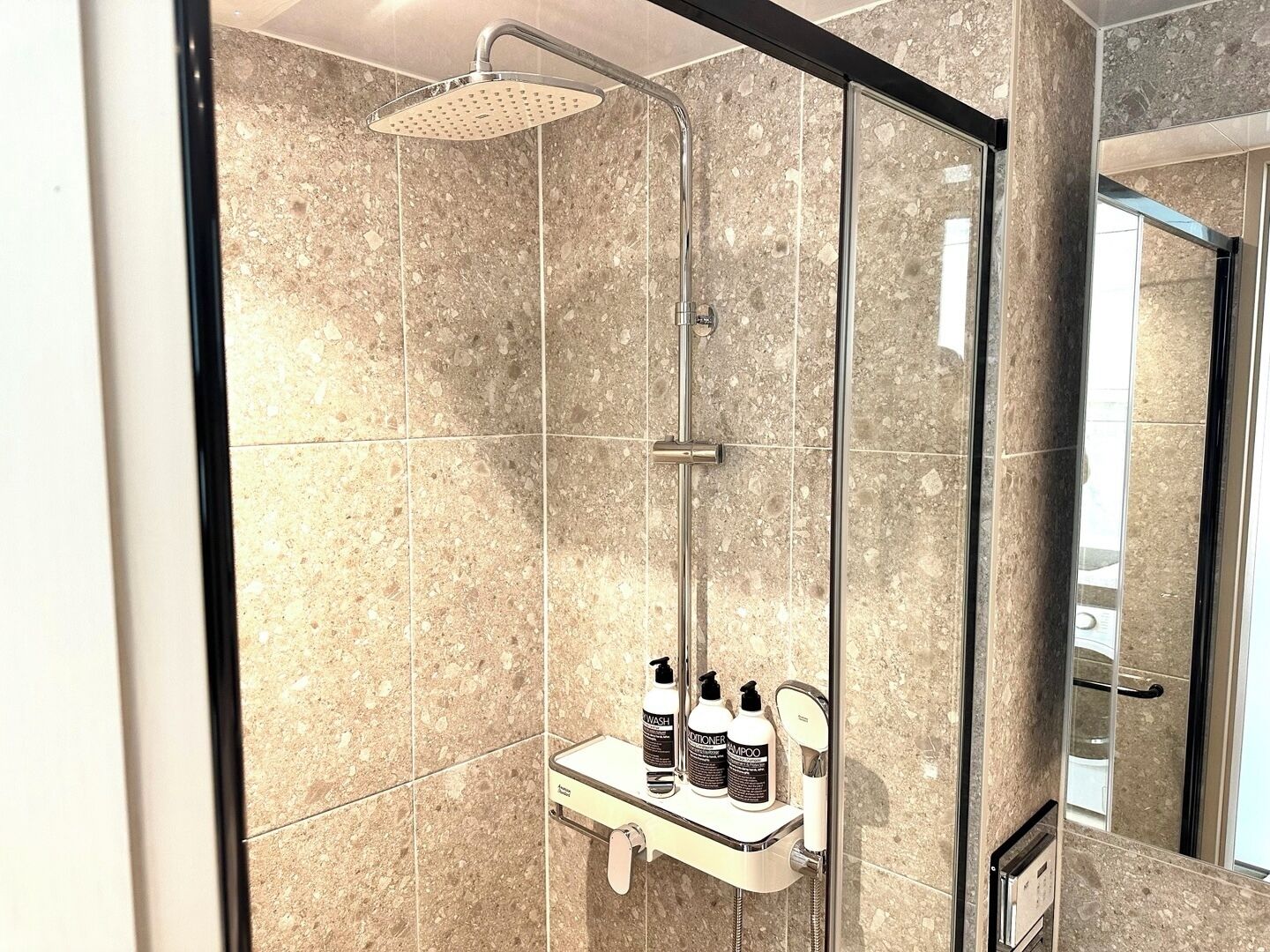 A modern bathroom with a glass-enclosed shower, marble tiles, and a vanity with toiletries.