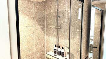 A modern bathroom with a glass-enclosed shower, marble tiles, and a vanity with toiletries.