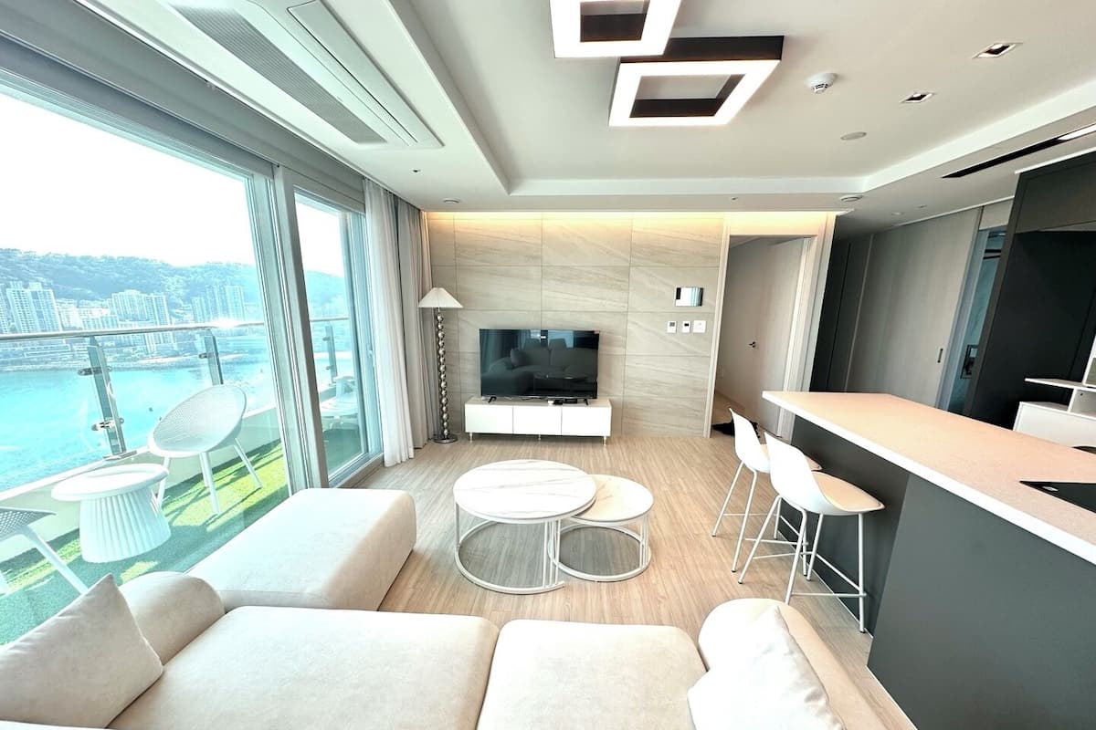 Una sala de estar moderna con un sofá, televisor, comedor y balcón con vistas a la ciudad.