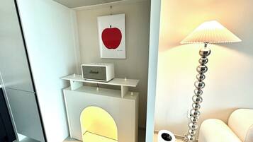 A modern, minimalist room with a white console table, a framed red apple artwork, a white lamp with a metallic base, and a white sofa.