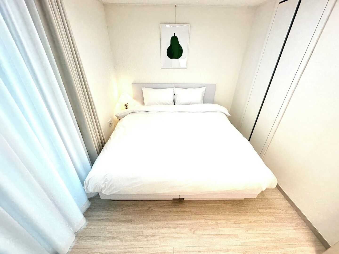 Una cama bien hecha en una habitación con piso de color claro y una única lámpara de pared.