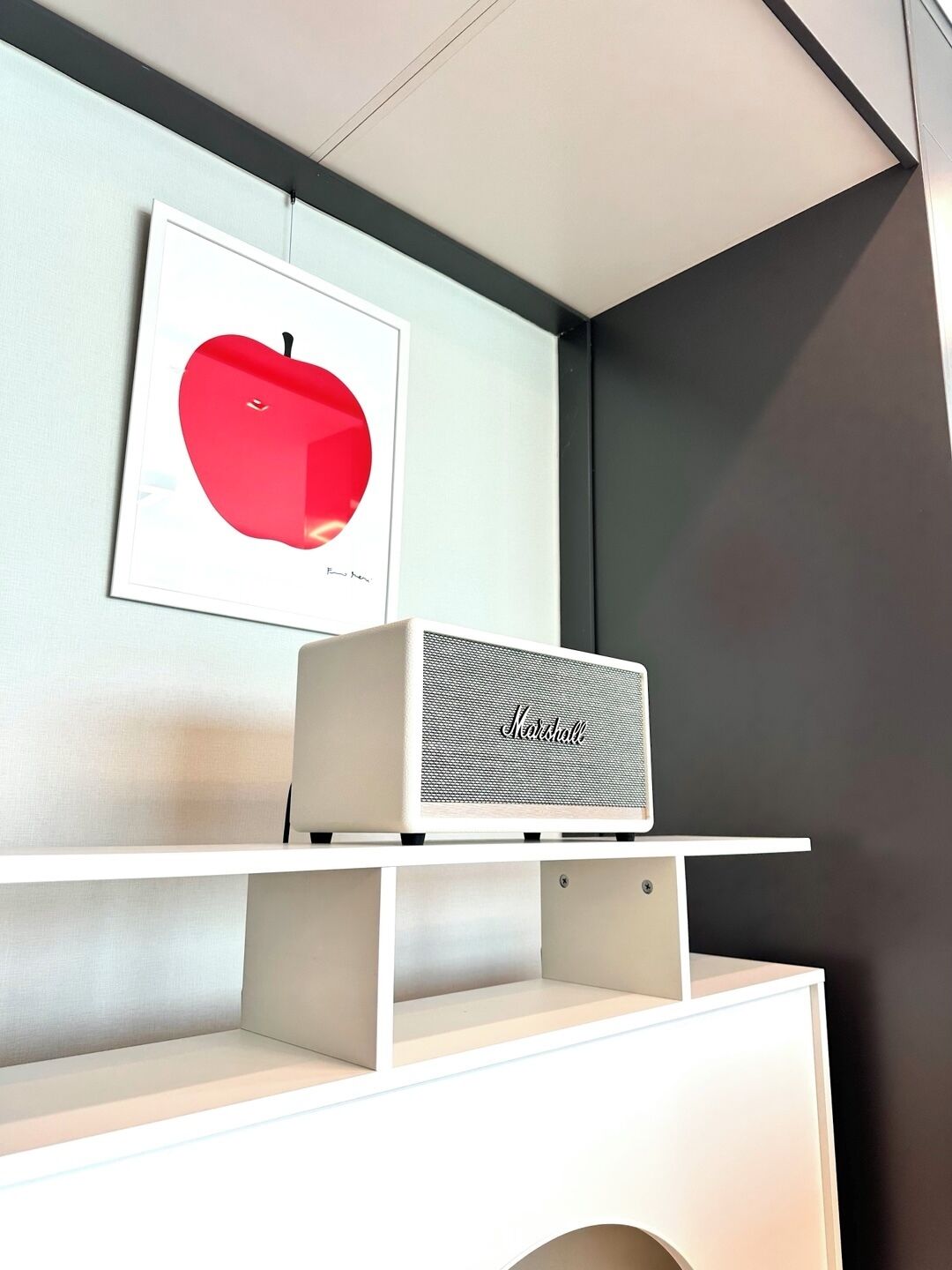 Een witte plank met een rode appel in een lijst en een witte Marshall-speaker.