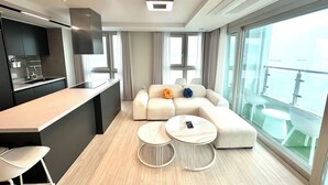 A modern living room with a sofa, two round tables, a kitchen area, and large windows offering a view. - THE DECEMBER STAY Busan Ocean Terrace (Busan)