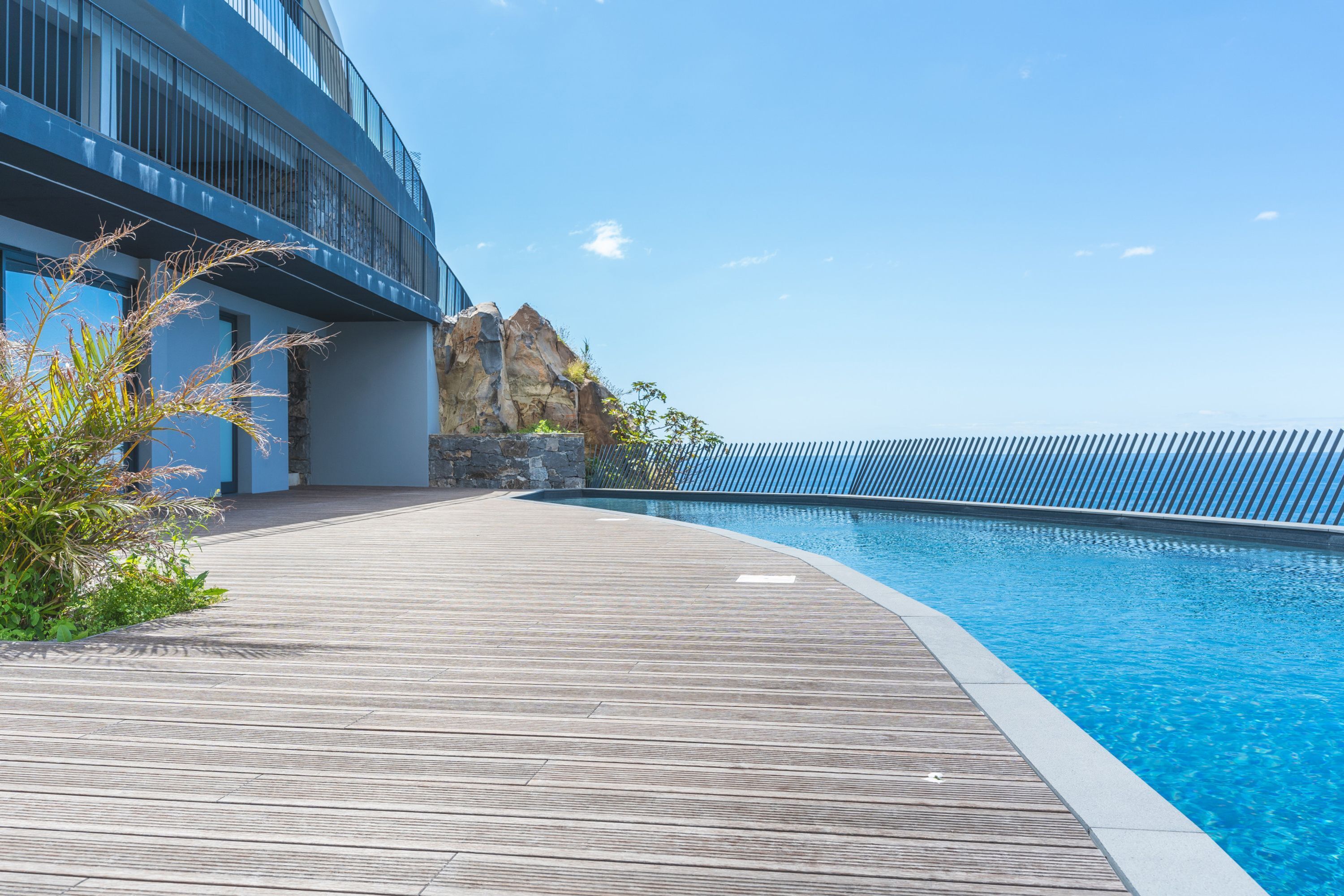 Un espace piscine moderne avec une terrasse en bois, une piscine à l’eau cristalline et un bâtiment doté de balcons.